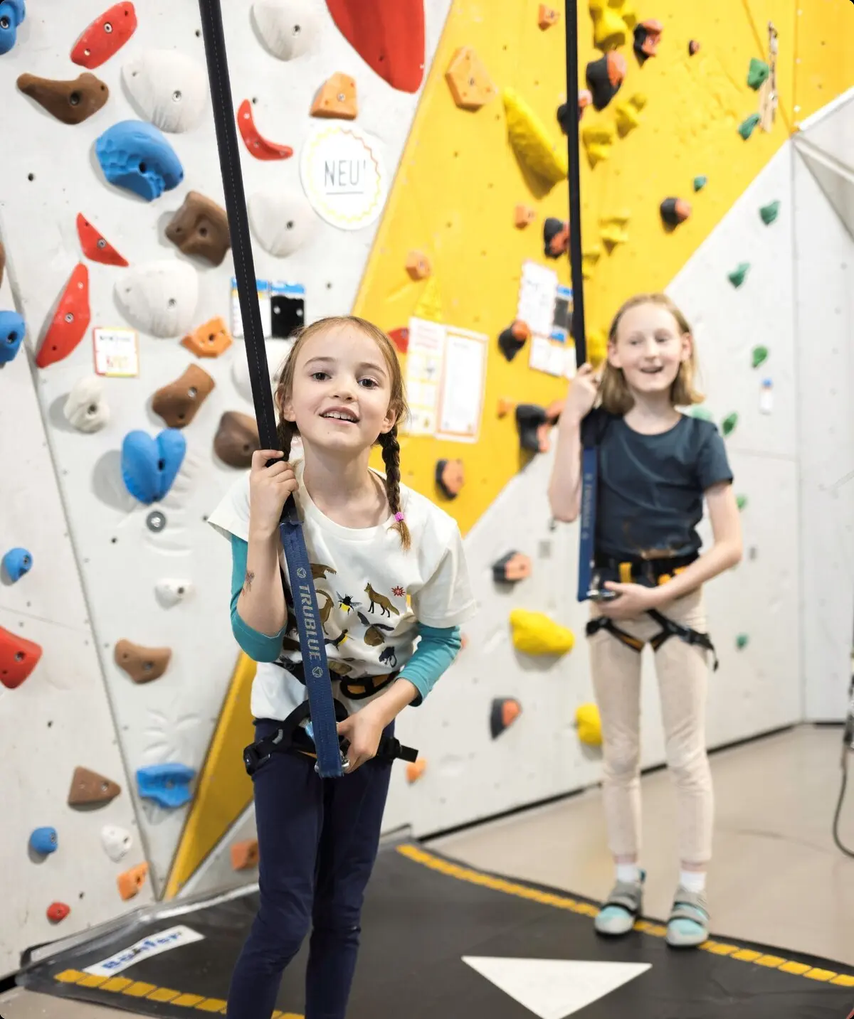 Zwei Mädchen kurz vor dem start in die Kletterwand - lachen freudig in die Kamera | © DAV / Jens Klatt