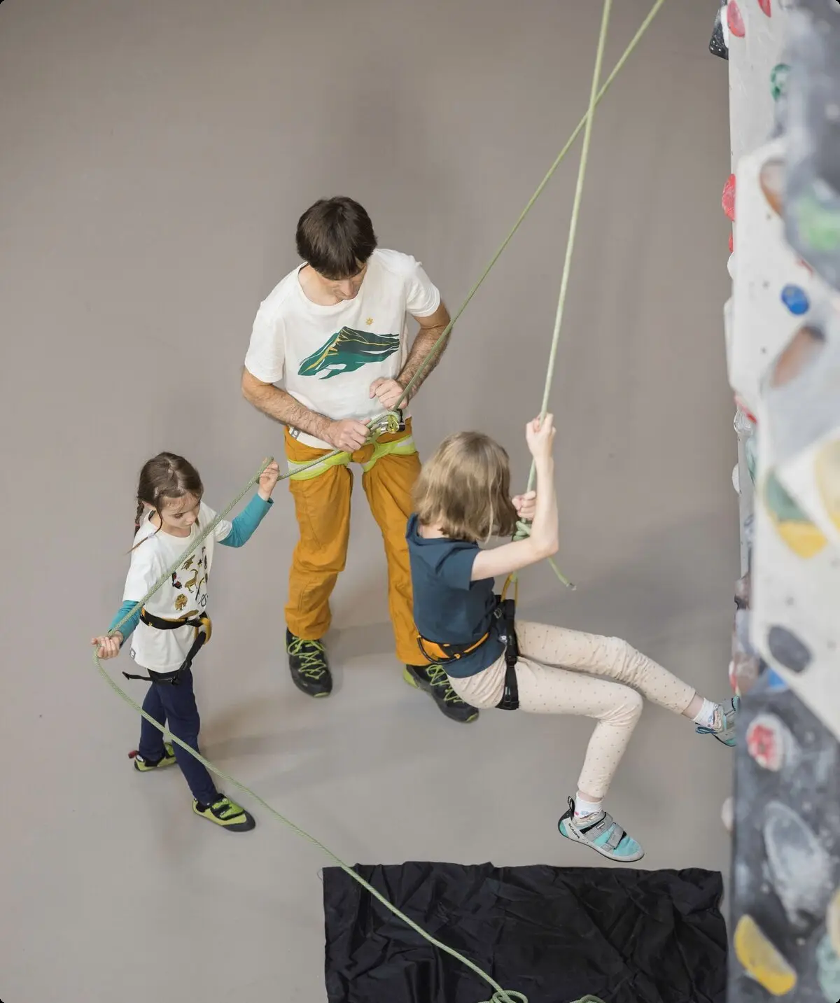 Ein Trainer und ein junges Mädchen sichern ein Kind beim Klettern | © DAV / Jens Klatt