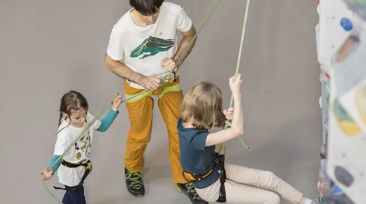 Ein Trainer und ein junges Mädchen sichern ein Kind beim Klettern | © DAV / Jens Klatt