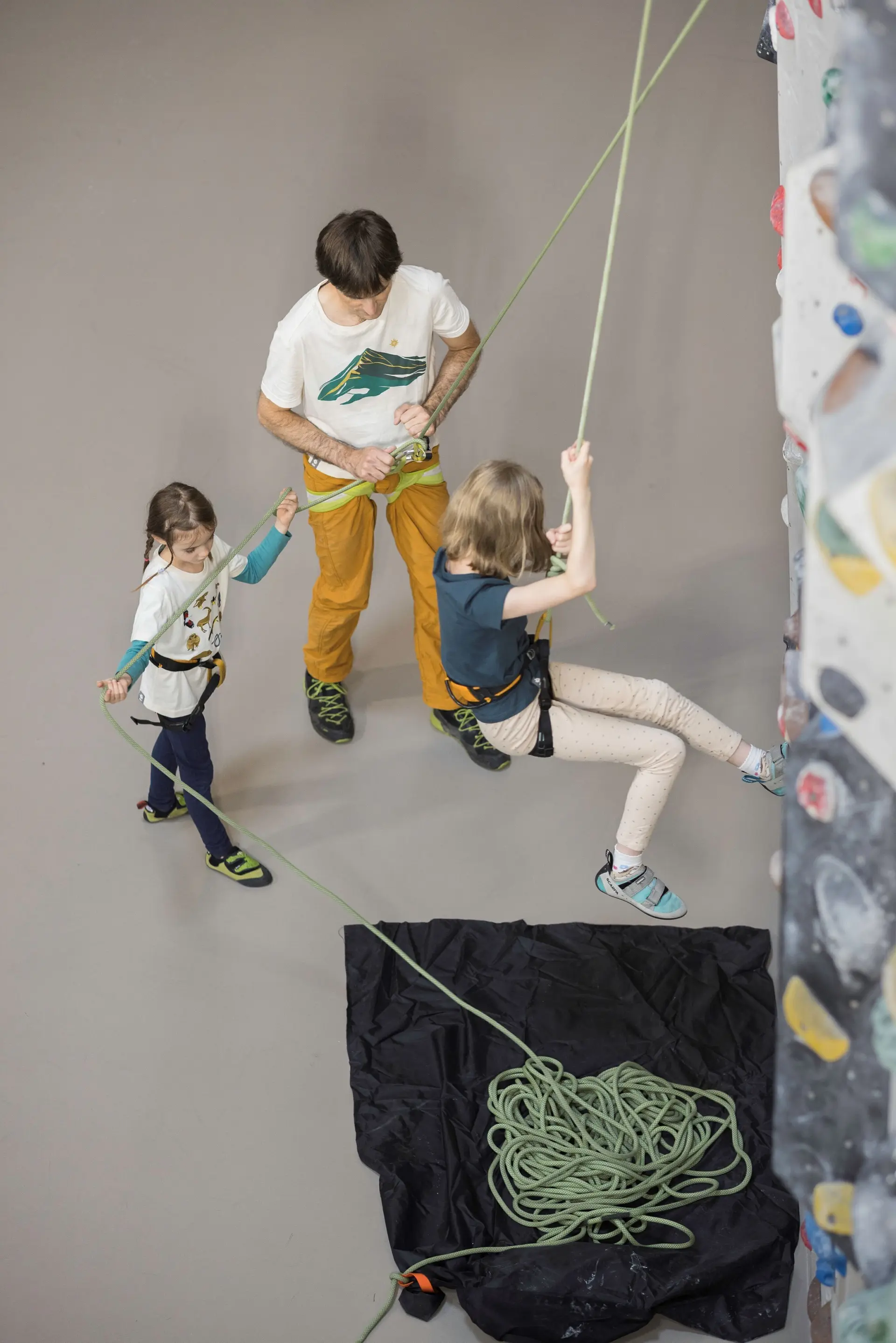 Ein Trainer und ein junges Mädchen sichern ein Kind beim Klettern | © DAV / Jens Klatt