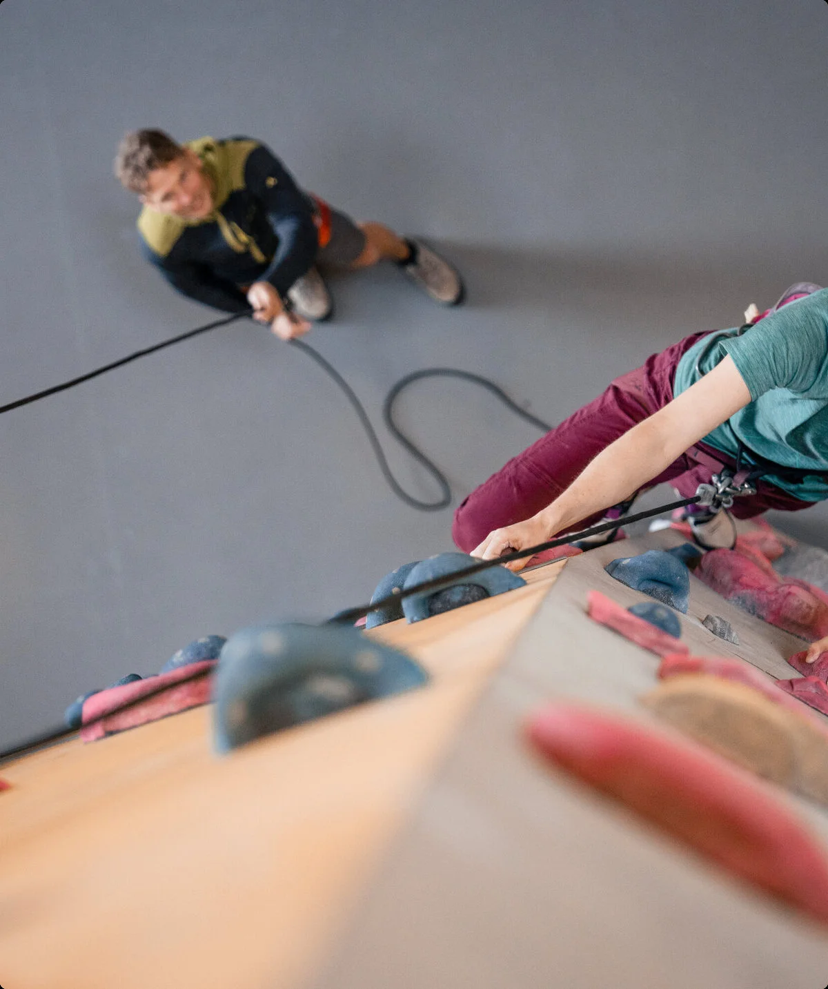 Eine Frau klettert in einer Kletterhalle, ihr Partner sichert sie. | © DAV / Julian Rohn